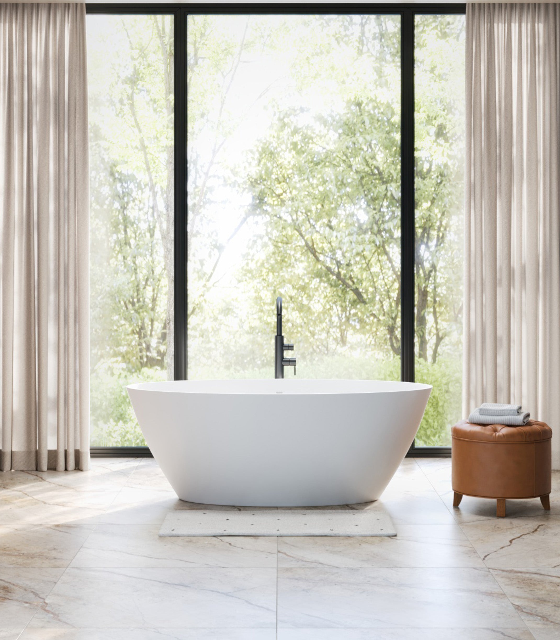 Modern white freestanding bathtub in a bright bathroom with large windows and a brown ottoman.