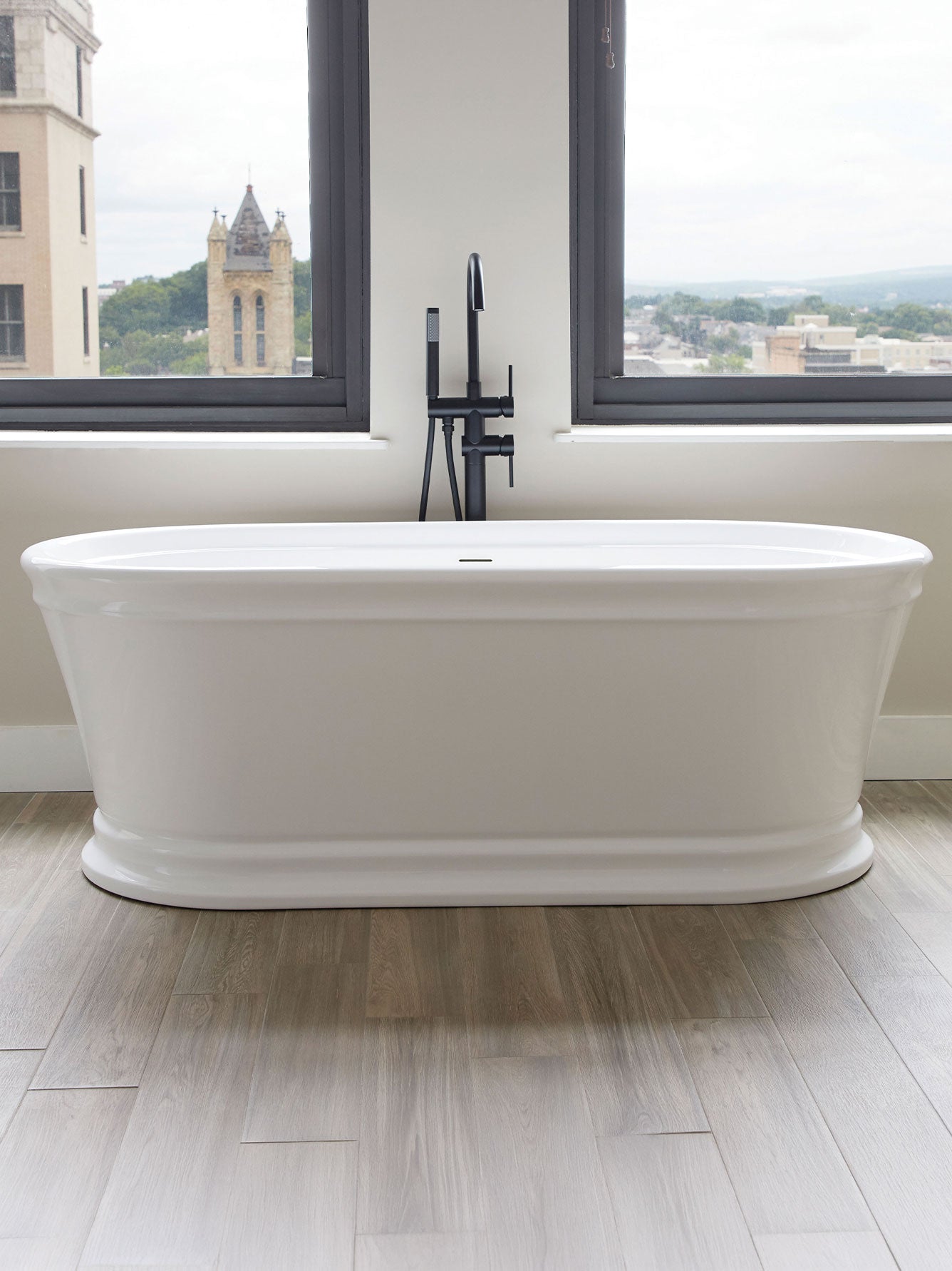 White freestanding bathtub in a modern bathroom with large windows.