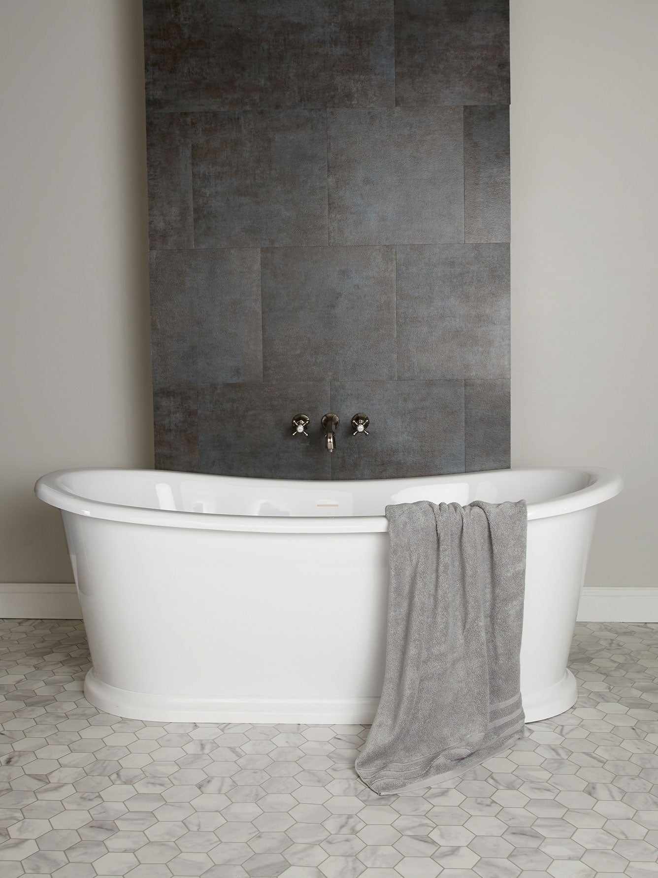 White freestanding bathtub with a gray towel against a dark tiled wall.