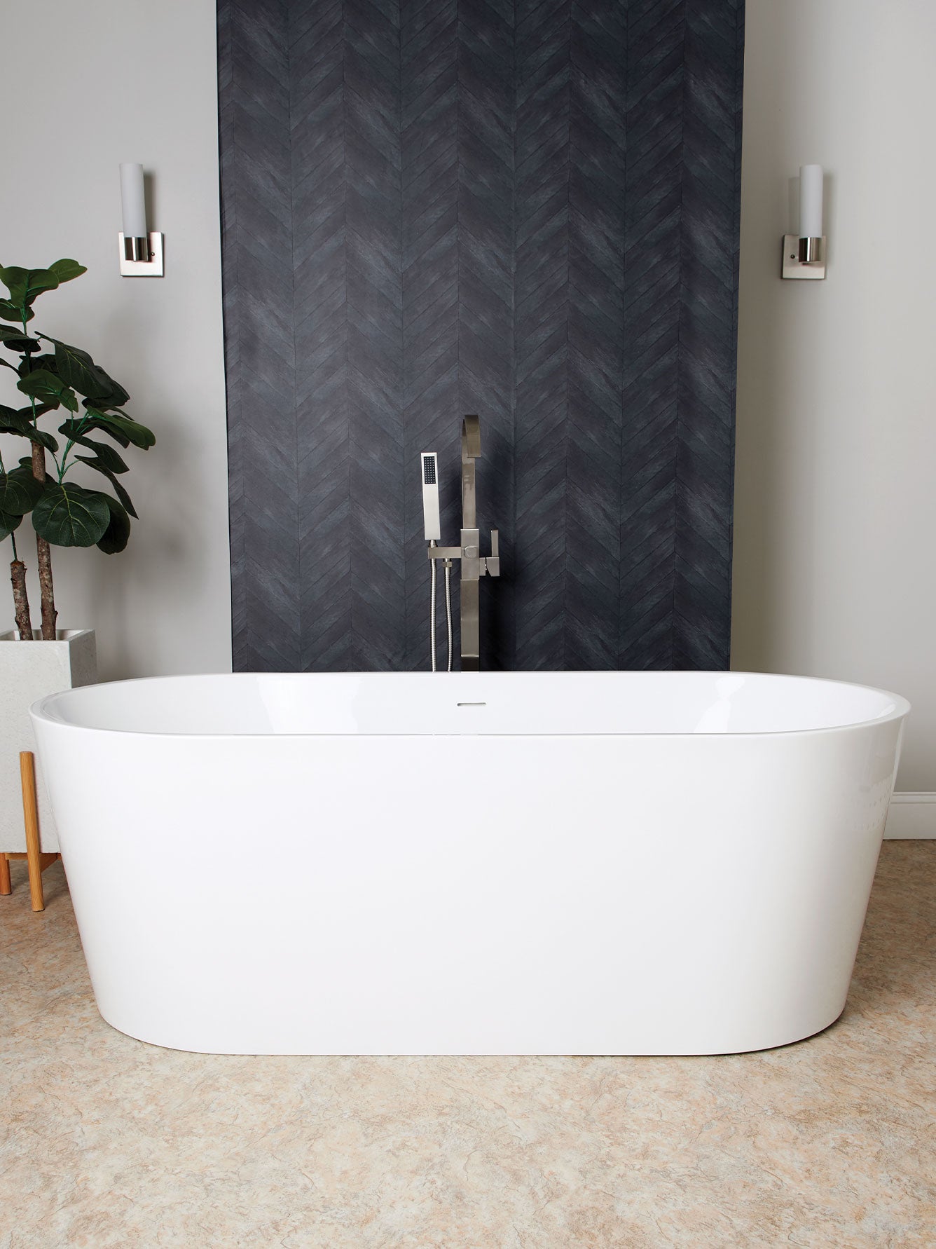 White freestanding bathtub in a modern bathroom with dark wall and plant.