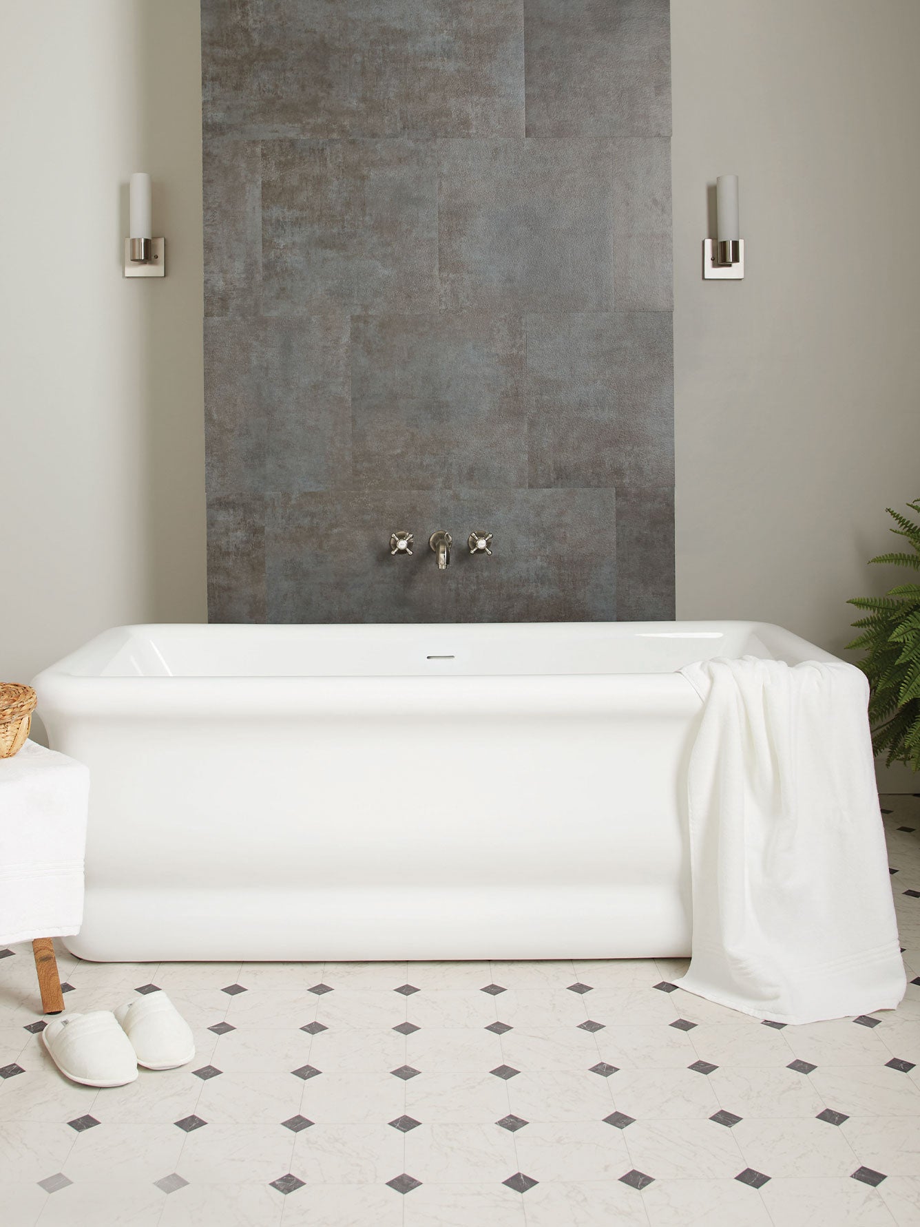 White freestanding bathtub in a bathroom with a gray tiled wall and patterned floor.