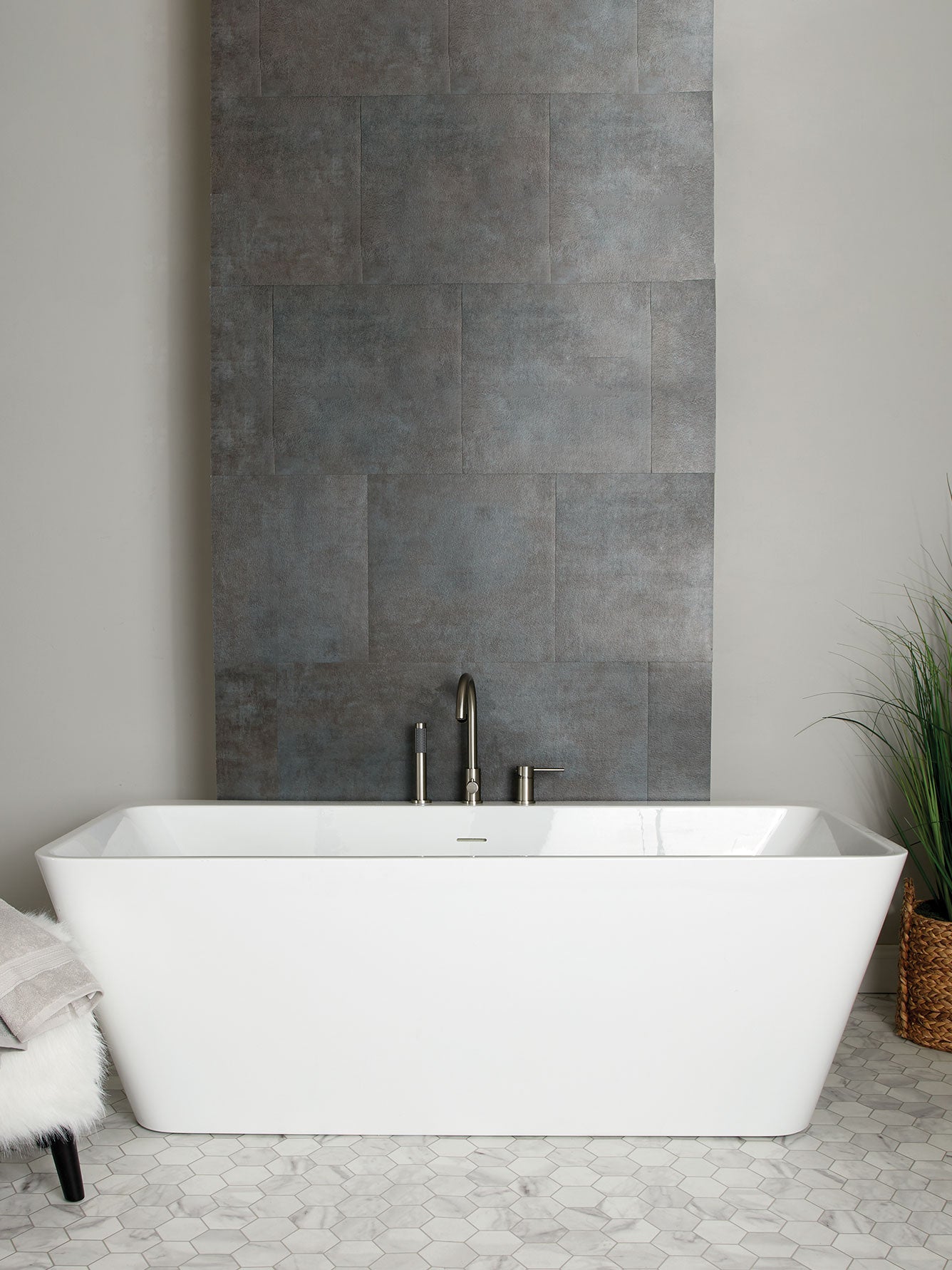 Modern bathroom with a freestanding white bathtub against a gray tiled wall.
