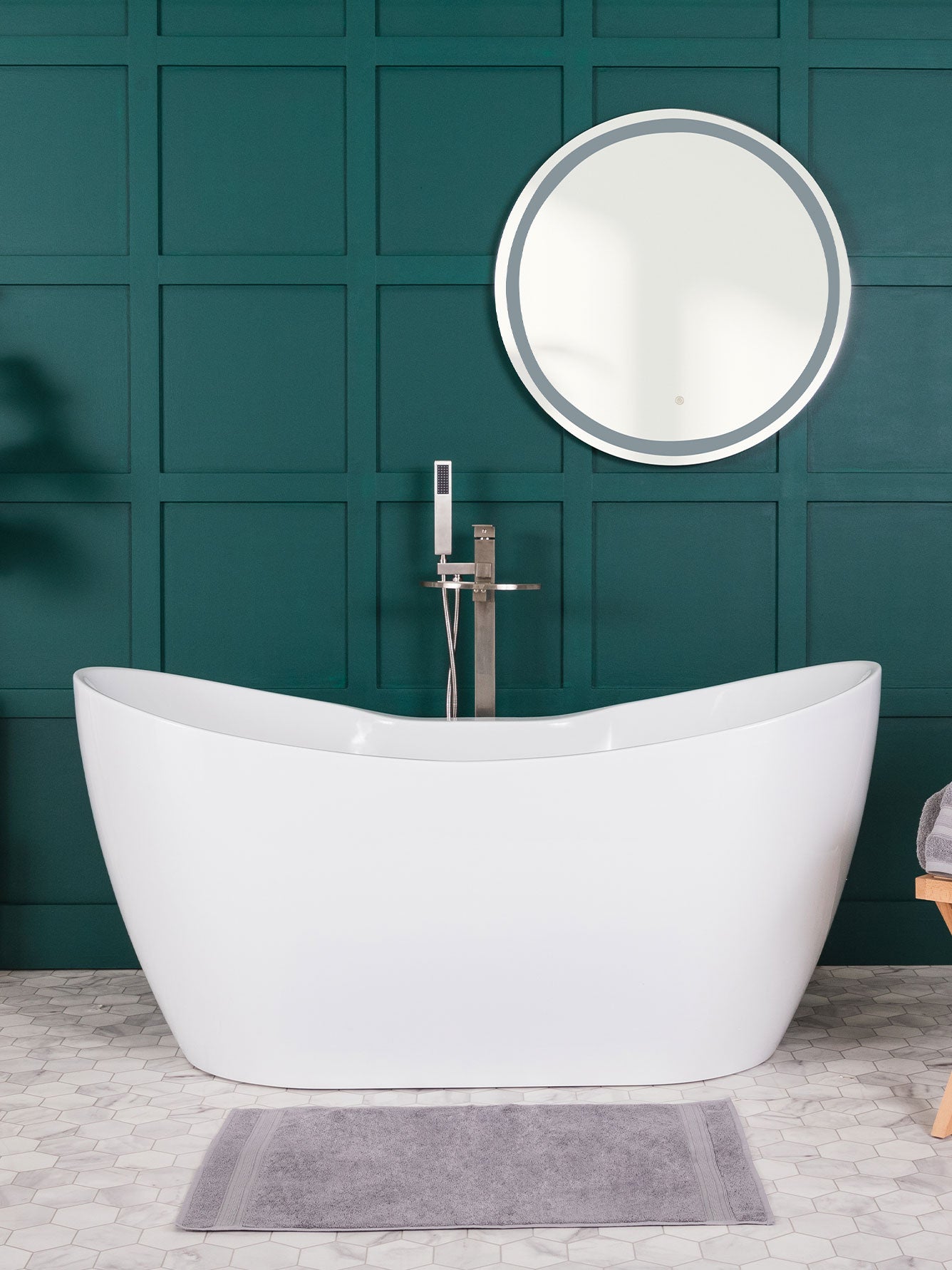White freestanding bathtub in a bathroom with a teal paneled wall and round mirror.