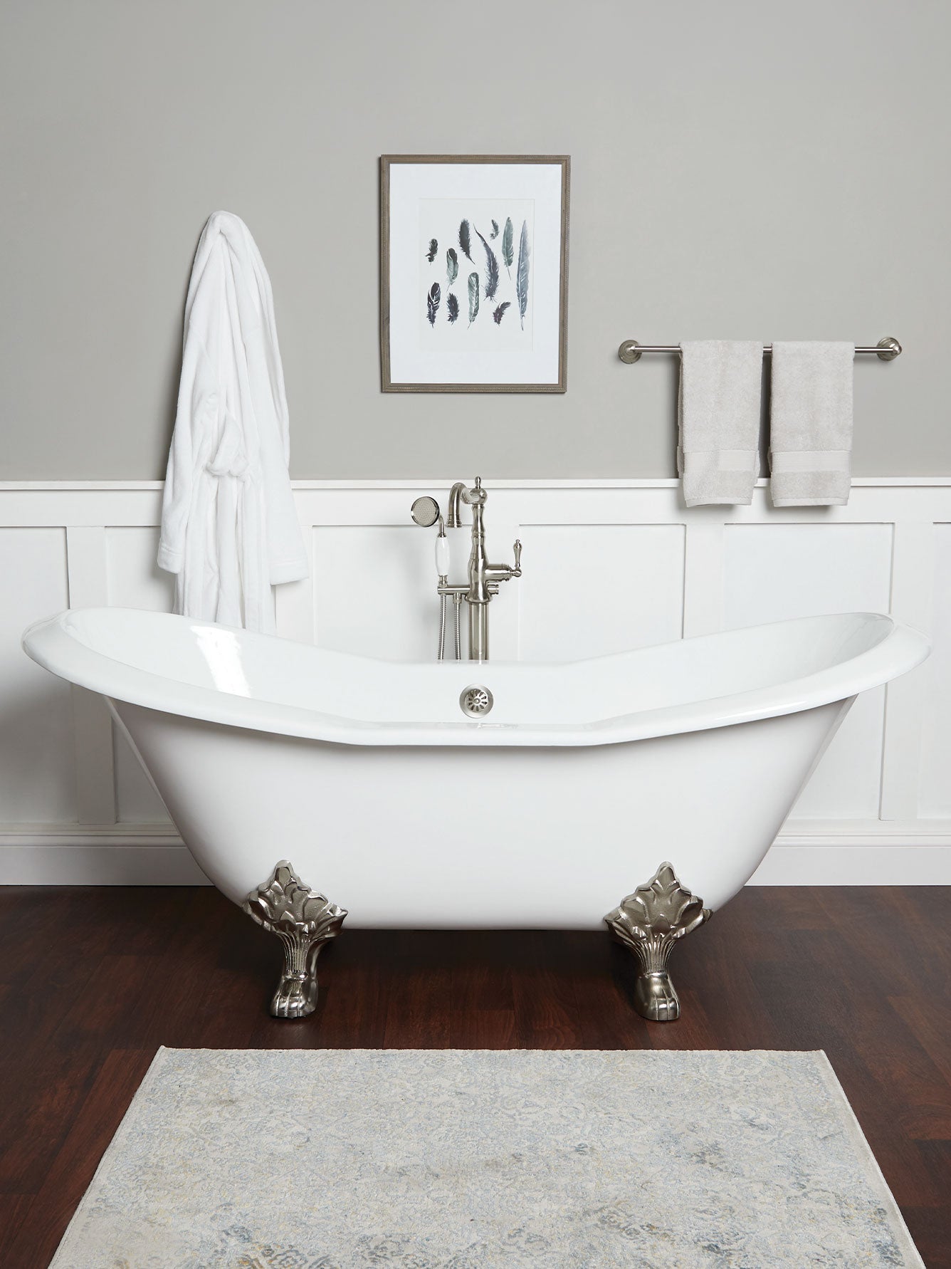 White freestanding bathtub in a bathroom with a gray wall and wooden floor.