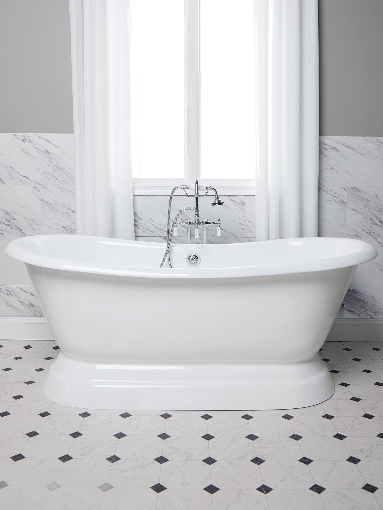 White freestanding bathtub in a bathroom with marble walls and floor.